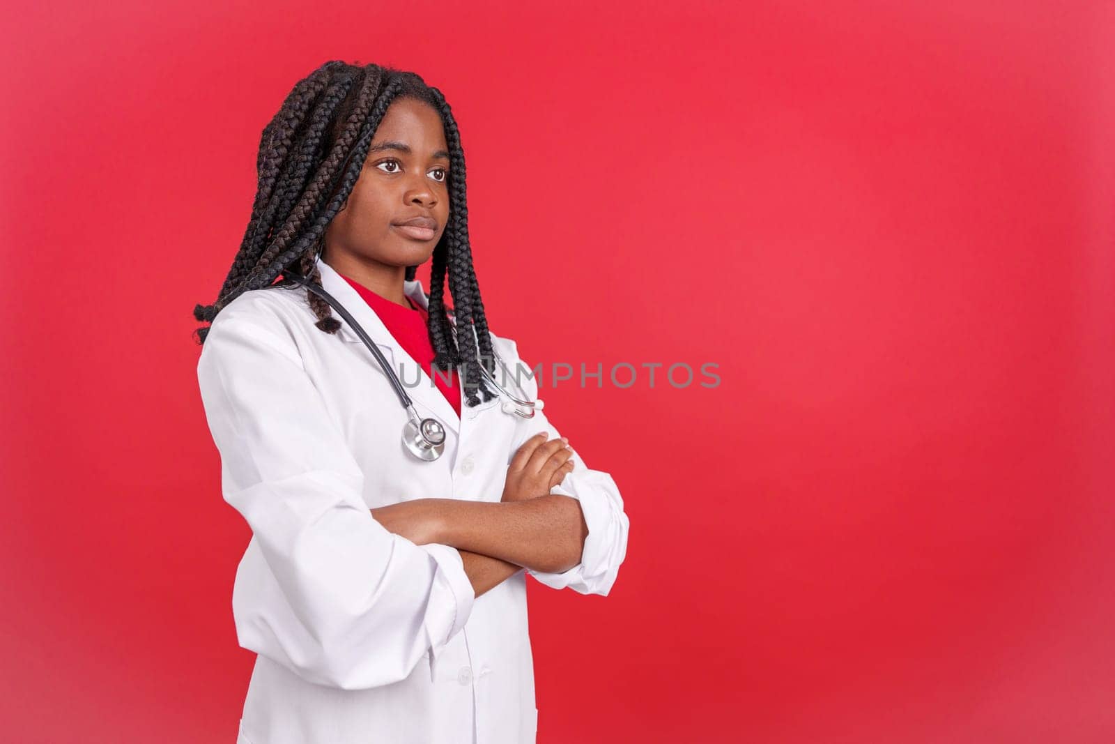 Serious african female doctor with arms crossed looking away in studio with red background