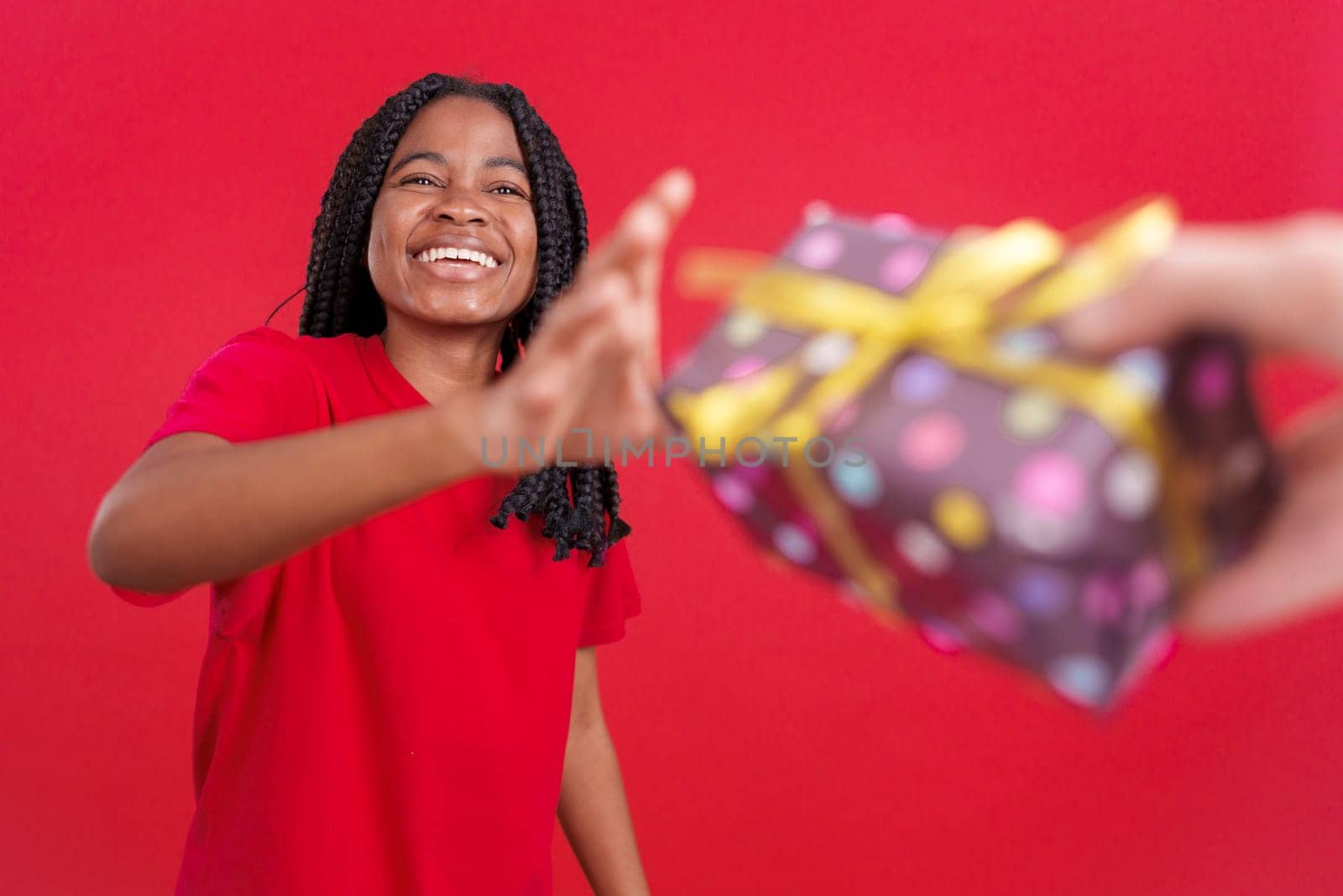 Happy african woman receiving a present from someone in studio with red background