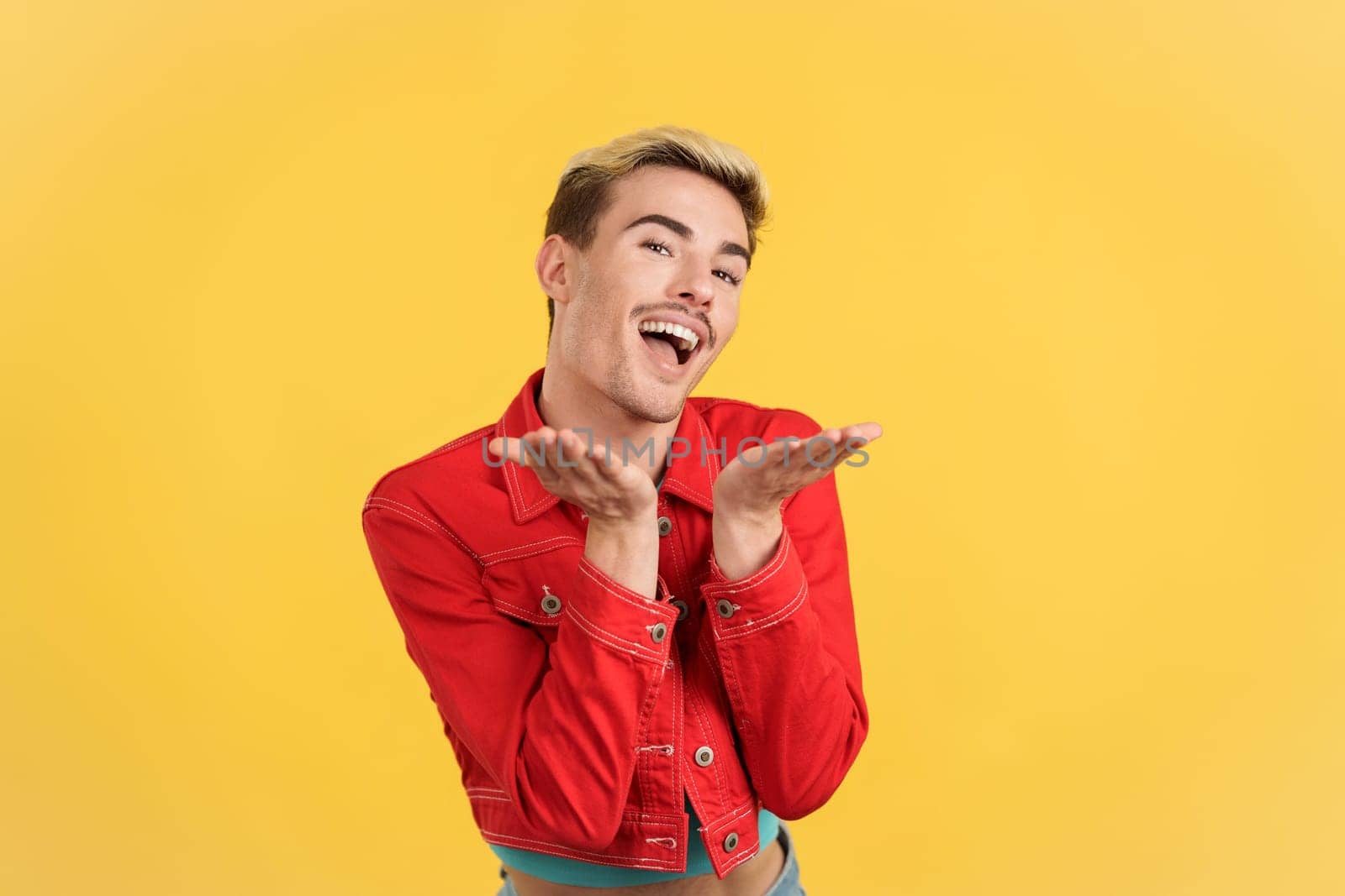 Gay man flirting while looking at camera and smiling in studio with yellow background