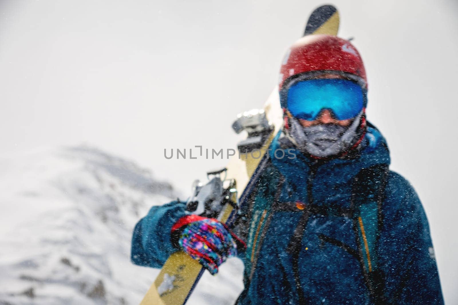 Defocused skier portrait during a snowstorm high in the mountains. Focus on the snow particles in front of the skier. Copy space top skier in blur.