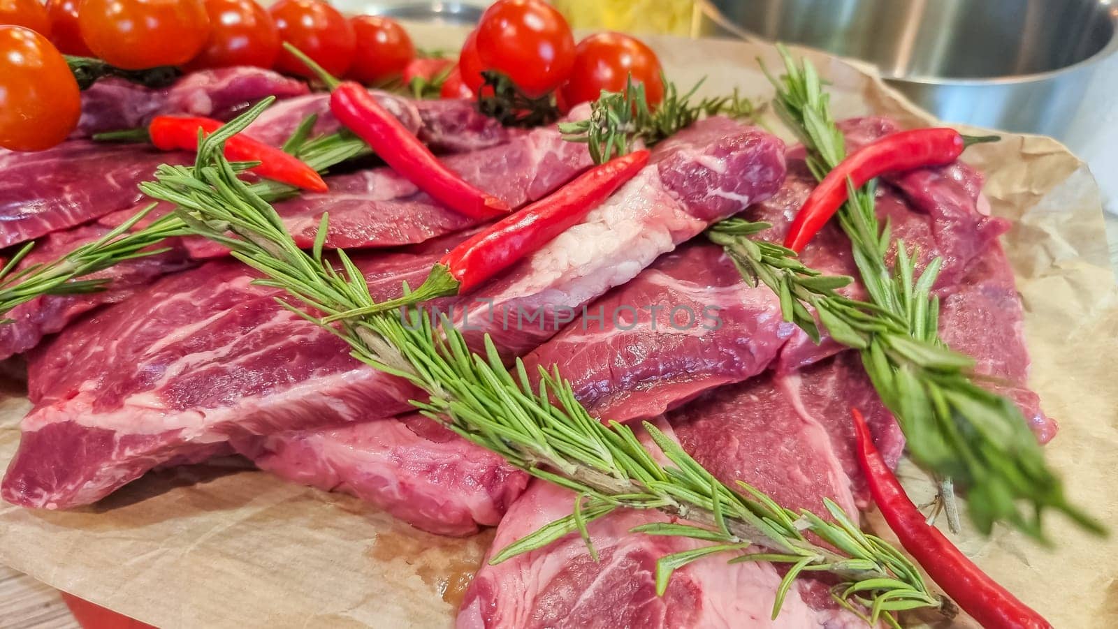 Aluminium foil roll with piece of raw meat, tomatoes, rosemary and spices on color wooden table, closeup