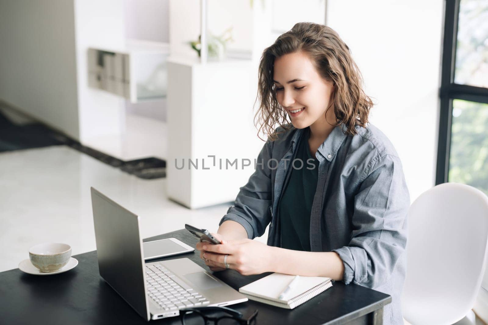 Young Woman Embracing the Modern Work Environment: Using Laptop Computer and Mobile Phone at Office. Student Girl Engaged in Productive Work from Home. Freelancing, Business, E-Learning, by ViShark