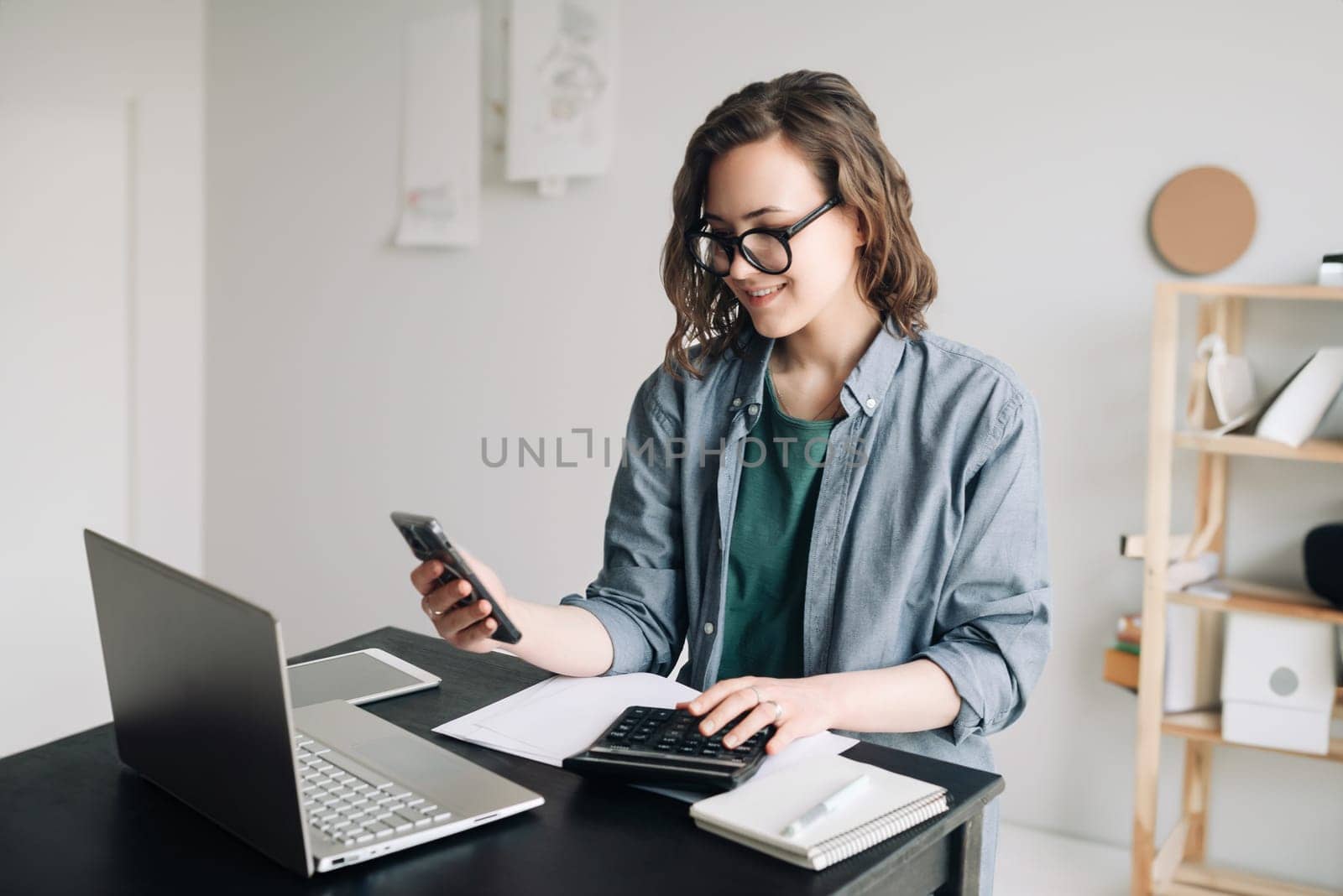 Professional woman accountant working with calculator and laptop computer in office. Smiling businesswoman working from home office. Finance and accounting concept, remote work, and business finance.