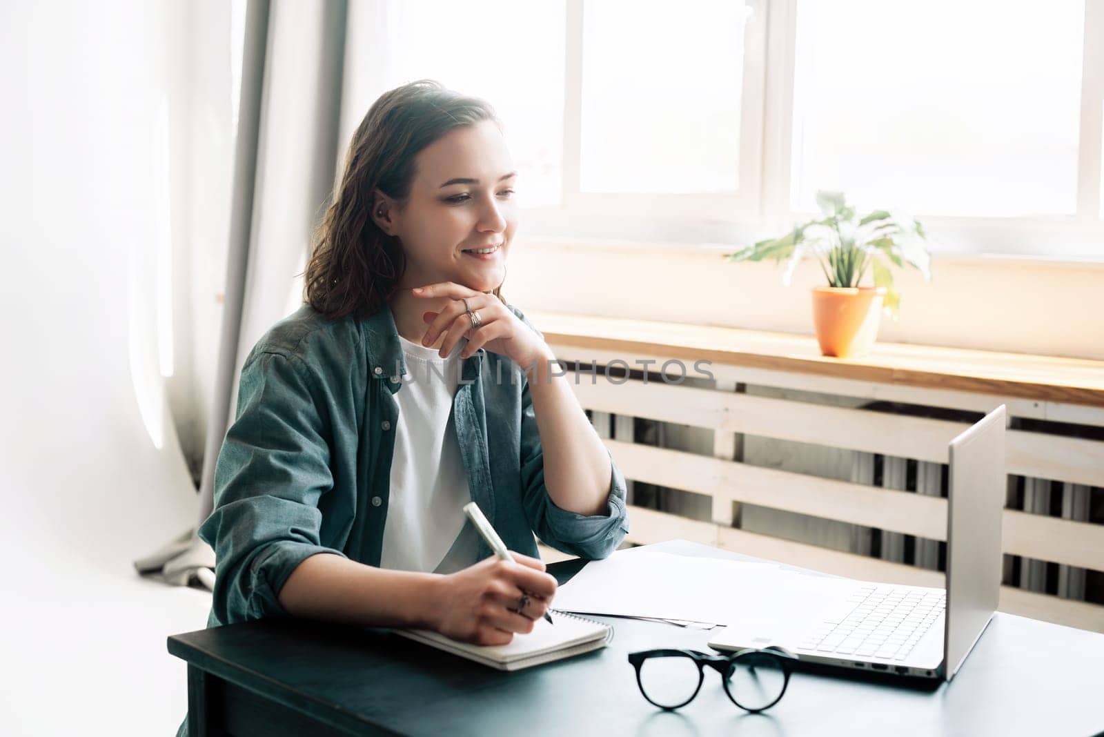 Young woman multitasking with laptop computer at office and student girl working remotely from home. Online work, study, freelance, and modern office lifestyle concept.