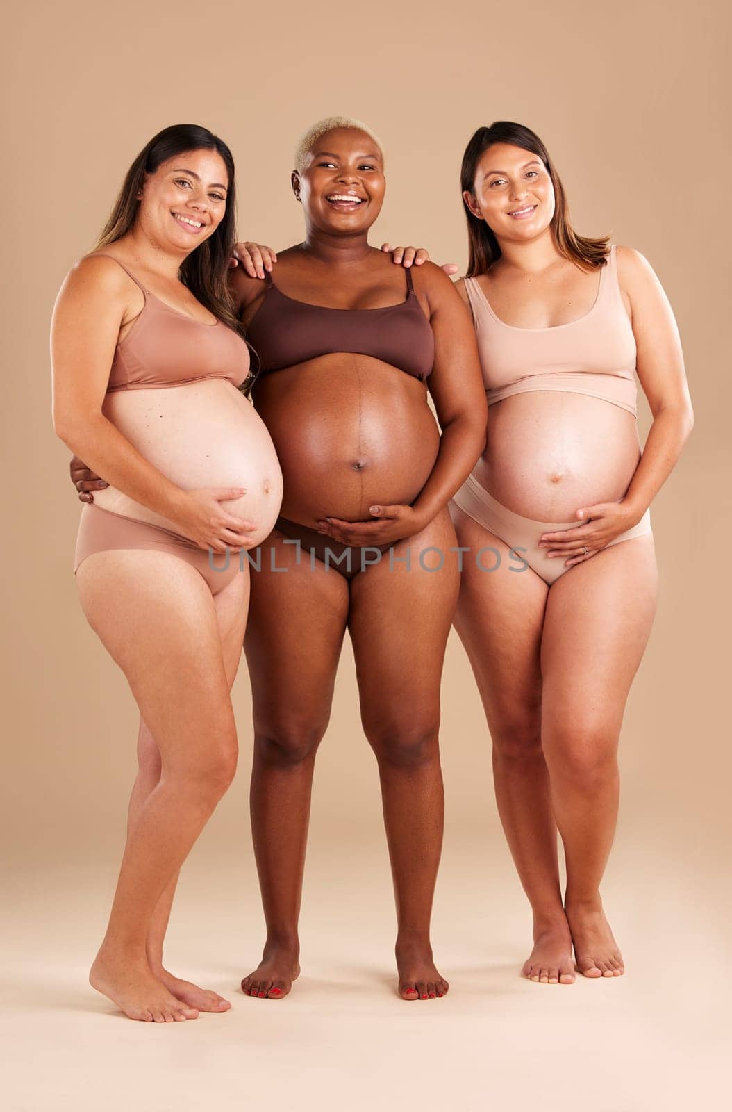 Pregnant, body and portrait of women in stomach support touch, hope and community diversity on studio background. Smile, happy and pregnancy friends in underwear, belly growth and healthcare wellness.