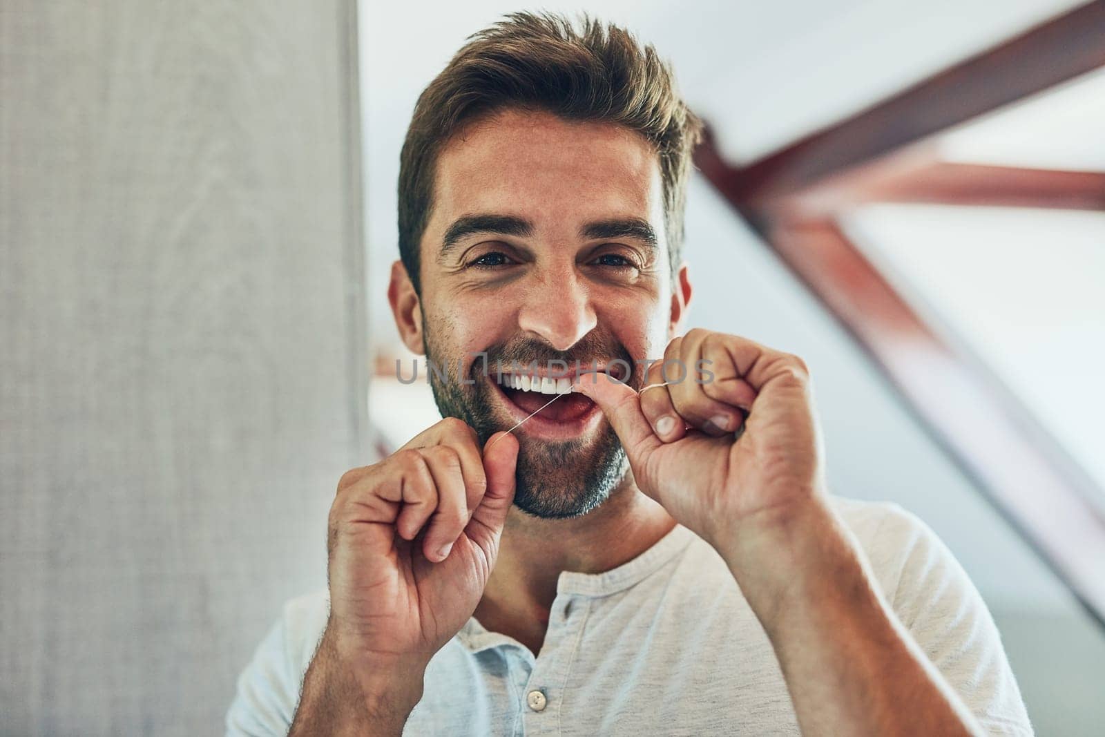 Pay attention to detail. Portrait of a cheerful young man flossing his teeth while looking at his reflection in the mirror at home. by YuriArcurs