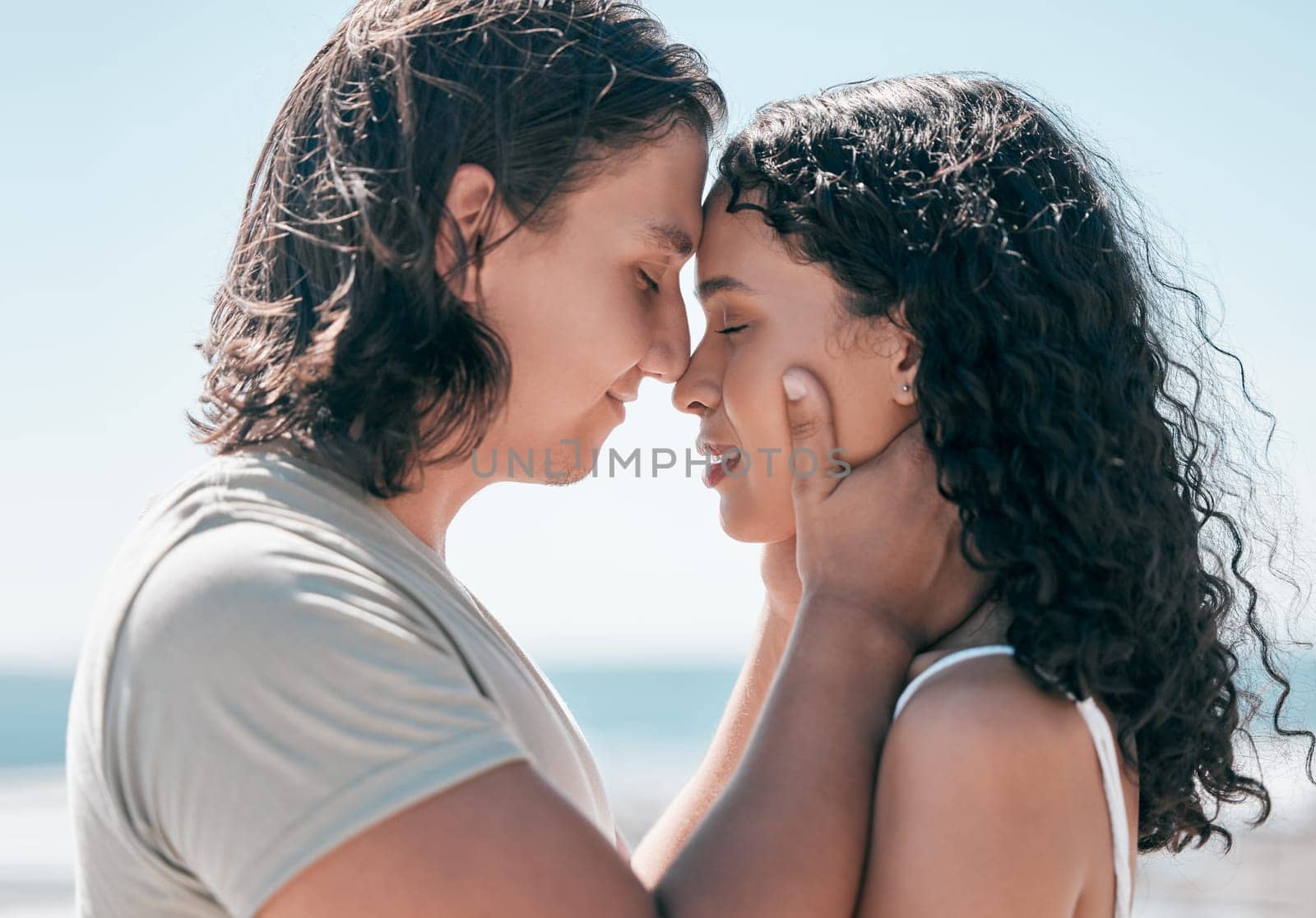 Love, hands on face and couple relax at a beach, in love and romantic on blue sky background. Intimate, moment and romance by man with woman on ocean trip, sweet and calm relationship moment in Bali.