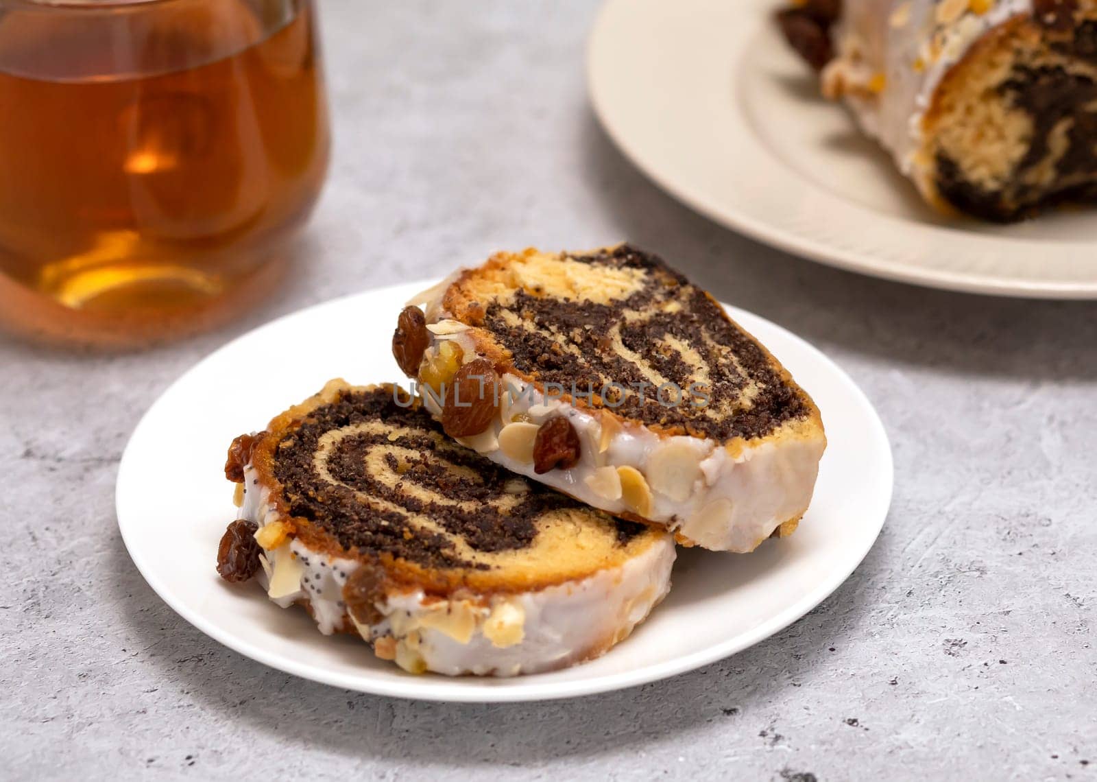 Slices of Christmas cake Makowiec with poppy seeds,traditional polish festive pie covered with sugar icing, walnuts, dried fruits on white background, cup of tea. Horizontal plane, close up