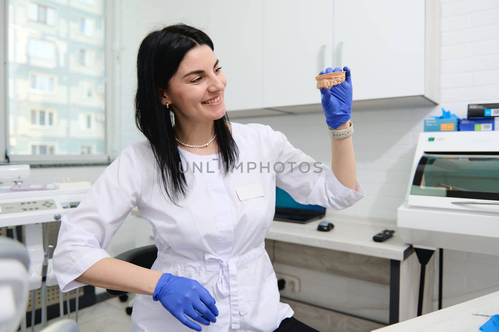 Professional experienced dentist woman, maxillofacial surgeon, prosthetic engineer, dental technician holding plaster cast of a human jaw model with teeth. Installing veneer or prosthetics in clinic