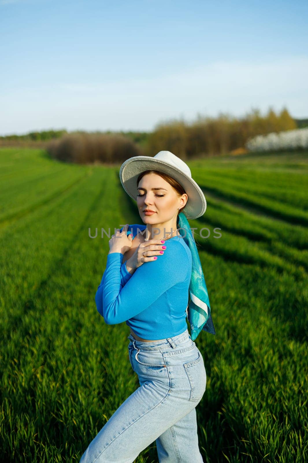 Young attractive woman in white hat, blue shirt, blue jeans, posing in summer green field. Copy, empty space for text