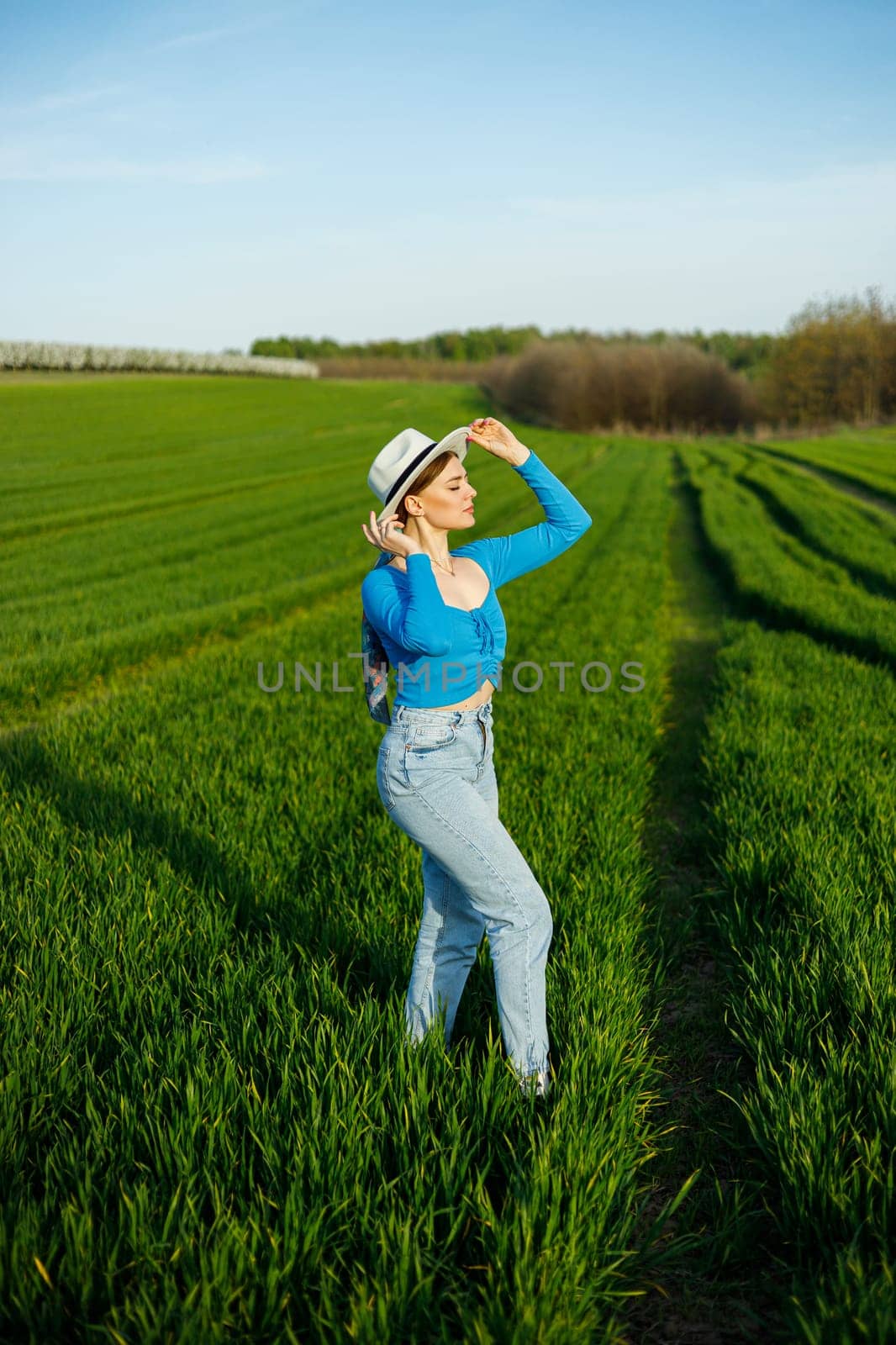 Young attractive woman in white hat, blue shirt, blue jeans, posing in summer green field. Copy, empty space for text