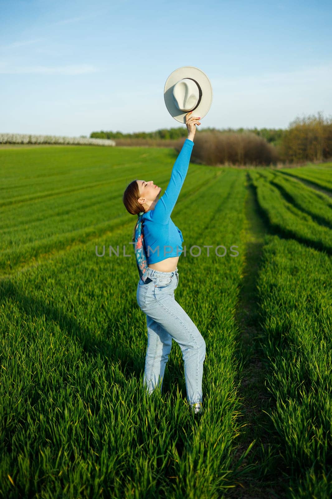 Young attractive woman in white hat, blue shirt, blue jeans, posing in summer green field. Copy, empty space for text