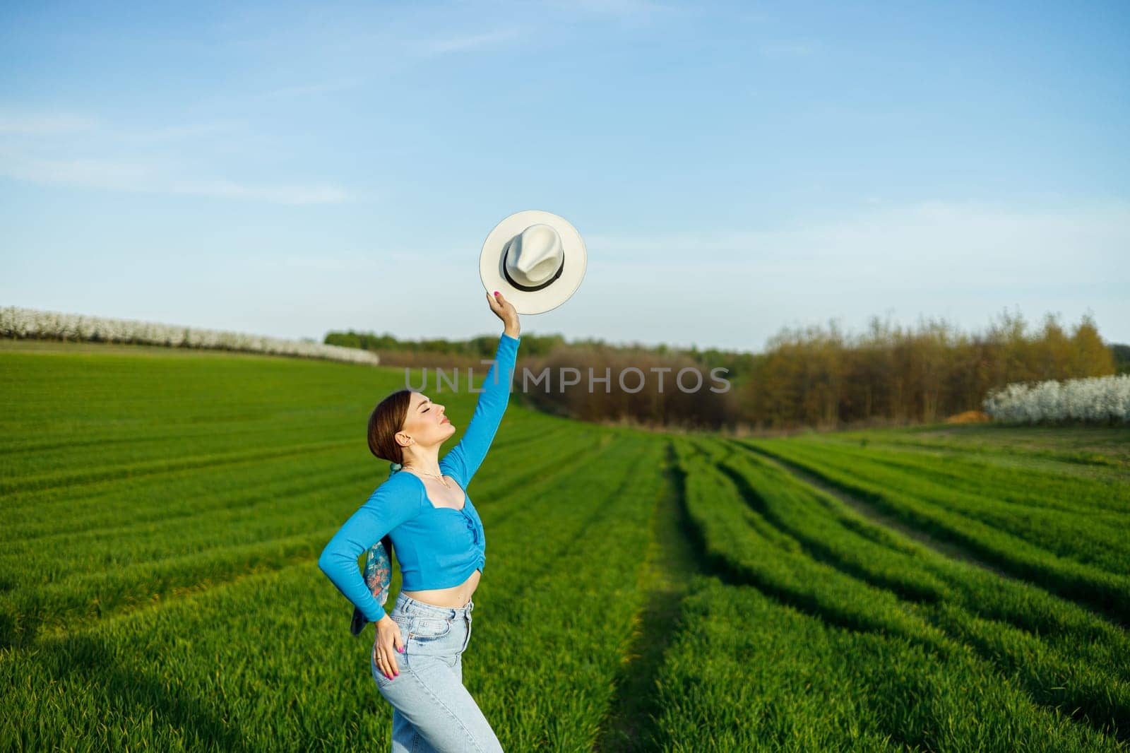 Young attractive woman in white hat, blue shirt, blue jeans, posing in summer green field. Copy, empty space for text