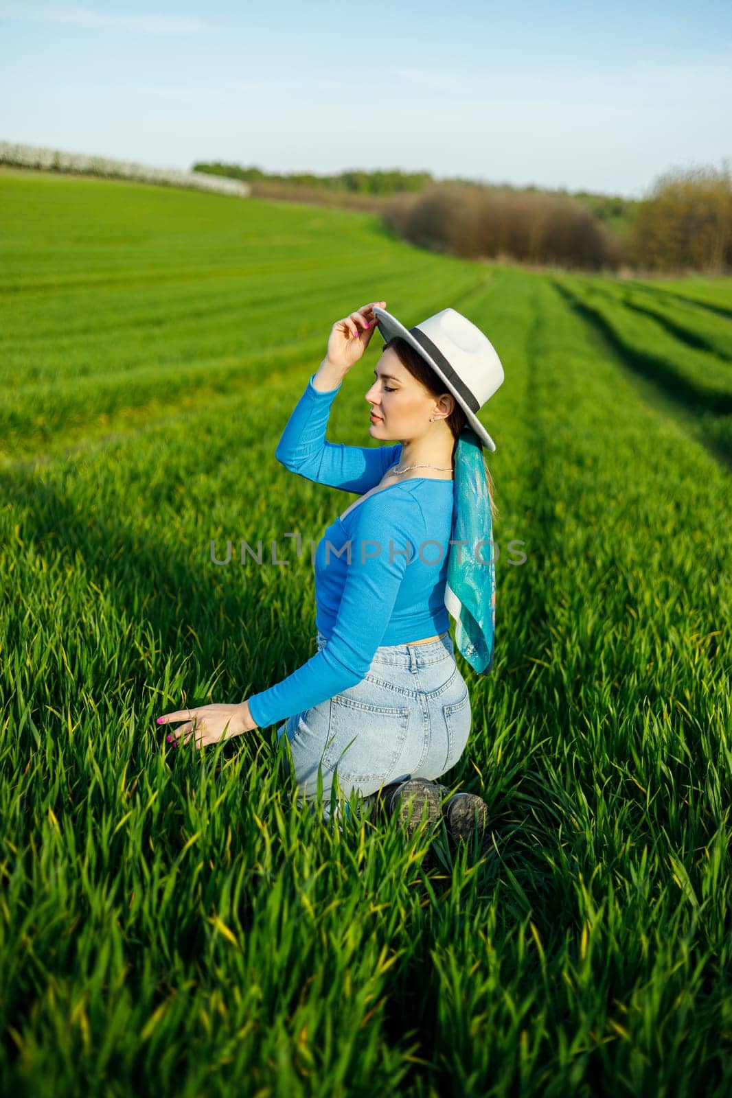 Young attractive woman in white hat, blue shirt, blue jeans, posing in summer green field. Copy, empty space for text