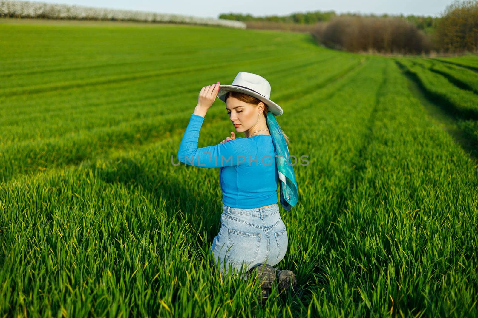 Young attractive woman in white hat, blue shirt, blue jeans, posing in summer green field. Copy, empty space for text