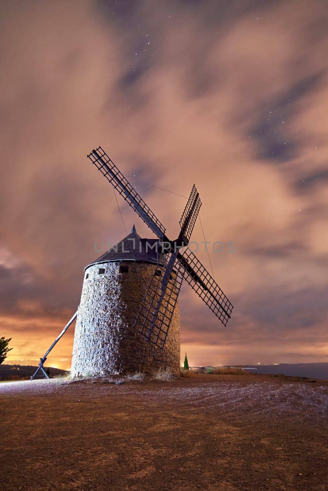 An old windmill in the night with clouds. Clouds on the run, night, warm colours, traditional construction, solitaire