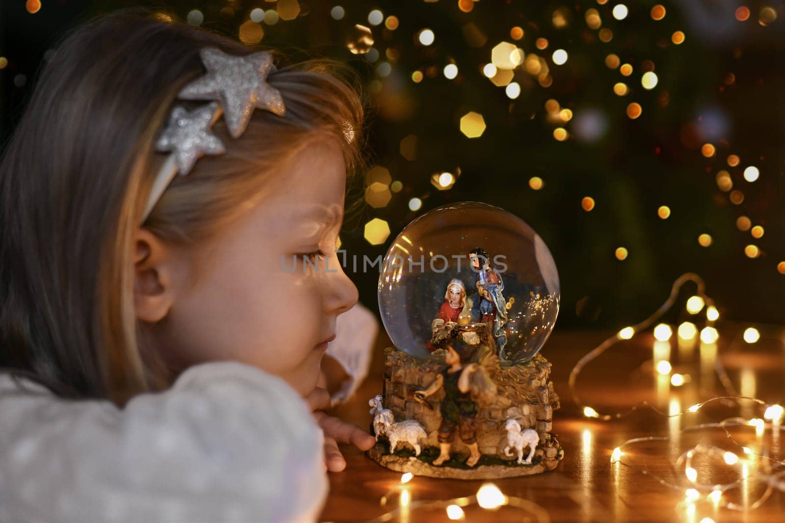 Girl looking at a glass ball with a scene of the birth of Jesus Christ near christmas tree