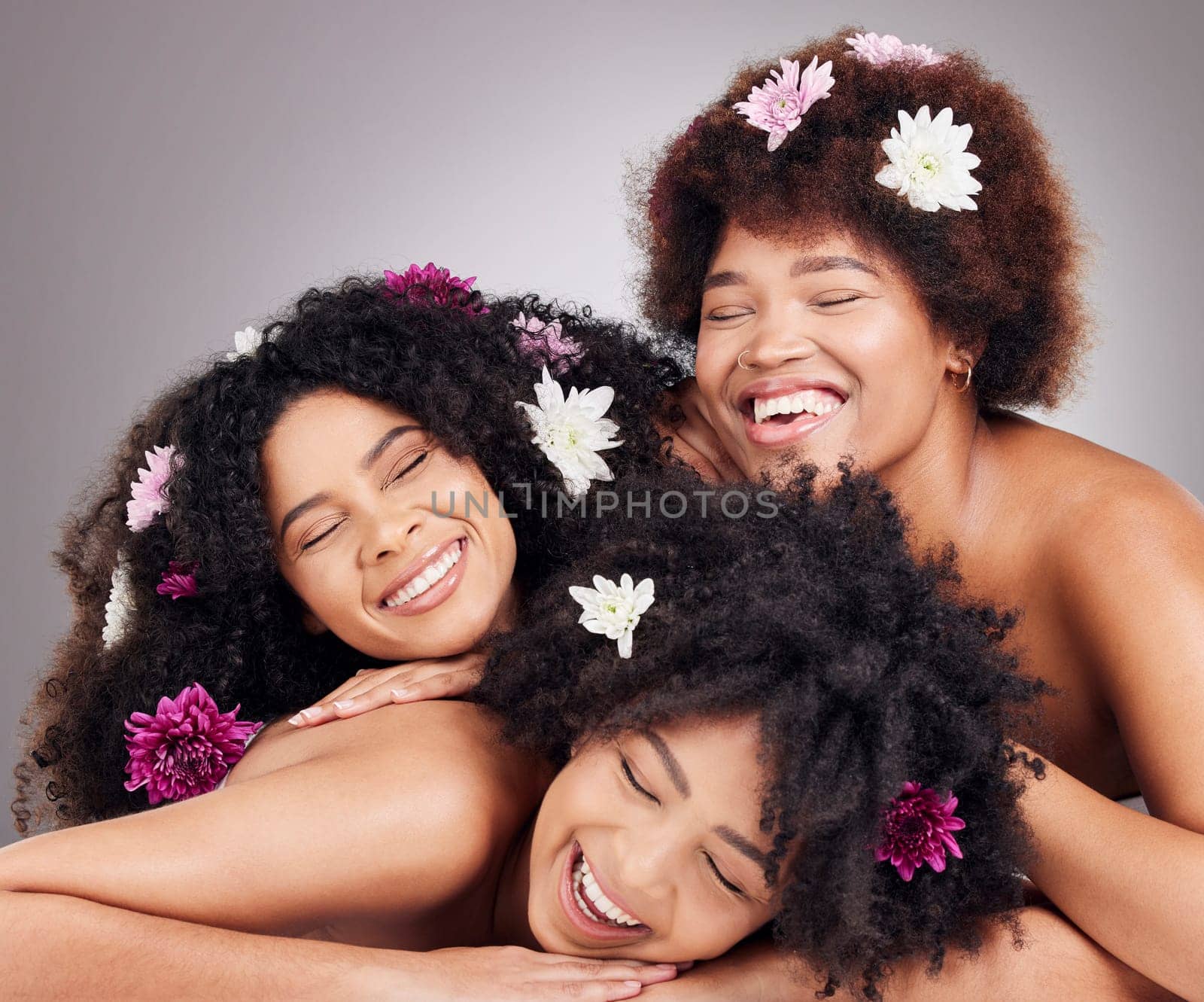 Friends, hair care and black women with flowers in studio isolated on a gray background. Floral cosmetics, organic makeup and face of group of girls or models with plants for aesthetic and beauty
