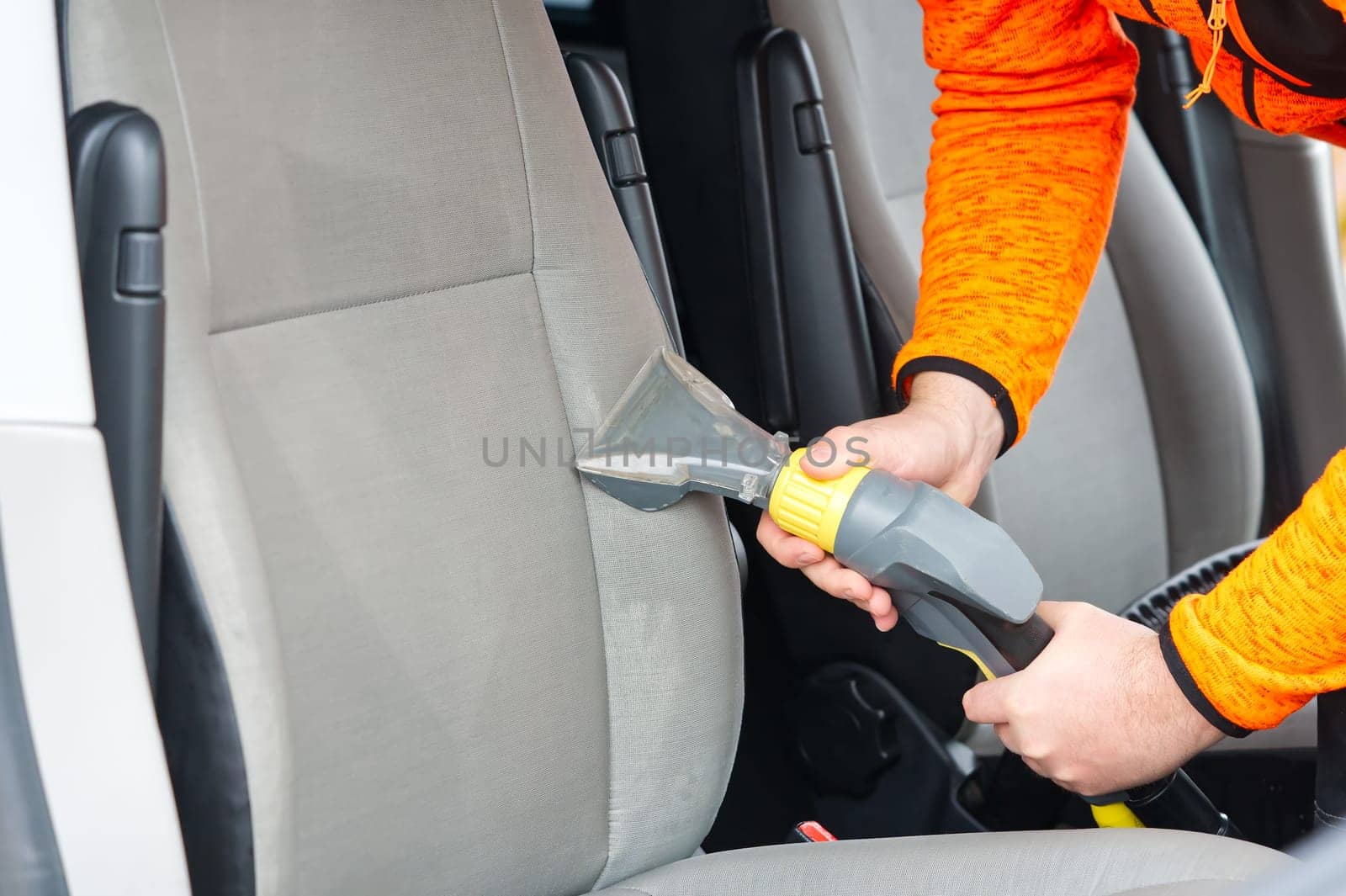 Handyman vacuuming car front textile seat with vacuum cleaner. man cleaning work Minivan.