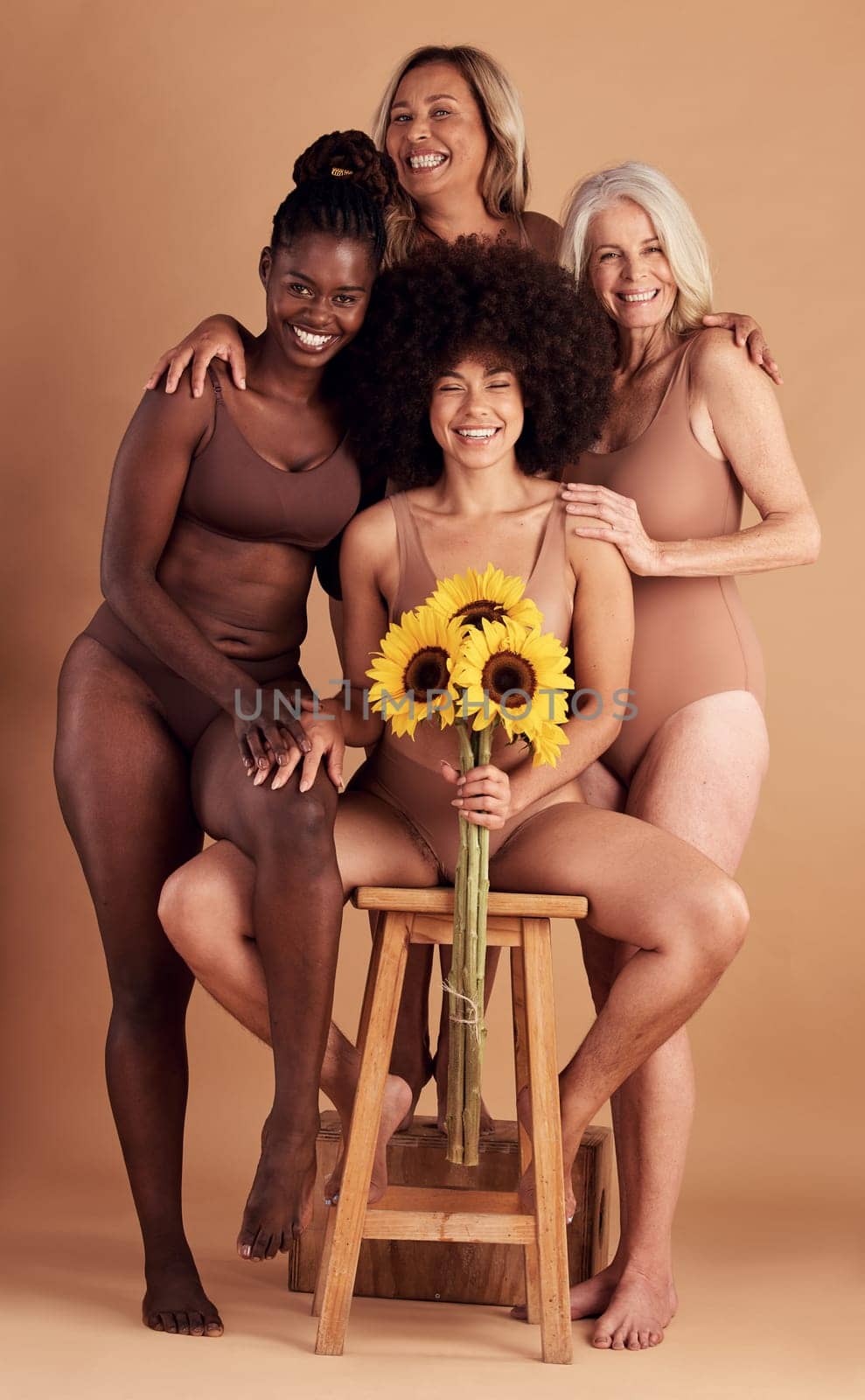 Plus size women, lingerie and group portrait with sunflower for beauty, wellness and solidarity in studio. Model team, underwear and flowers with support hug, diversity and smile by studio backdrop by YuriArcurs