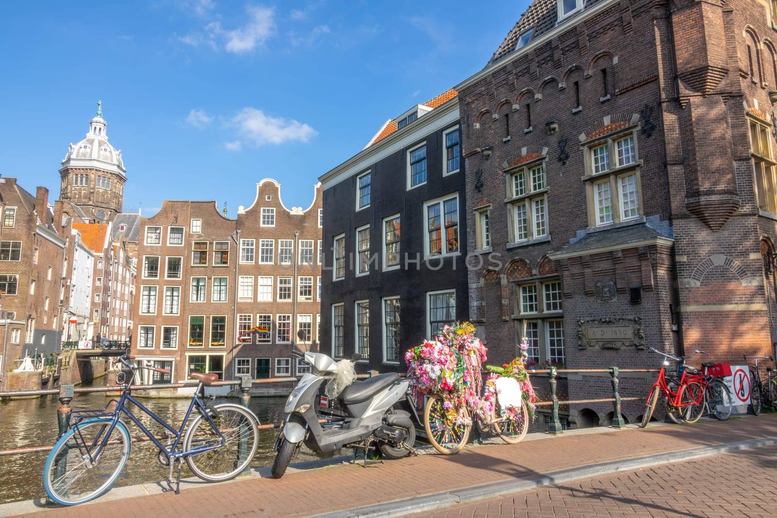 Netherlands. Summer day in Amsterdam. Scooter and bicycles near the railing of the bridge over the canal. Typical houses by the water