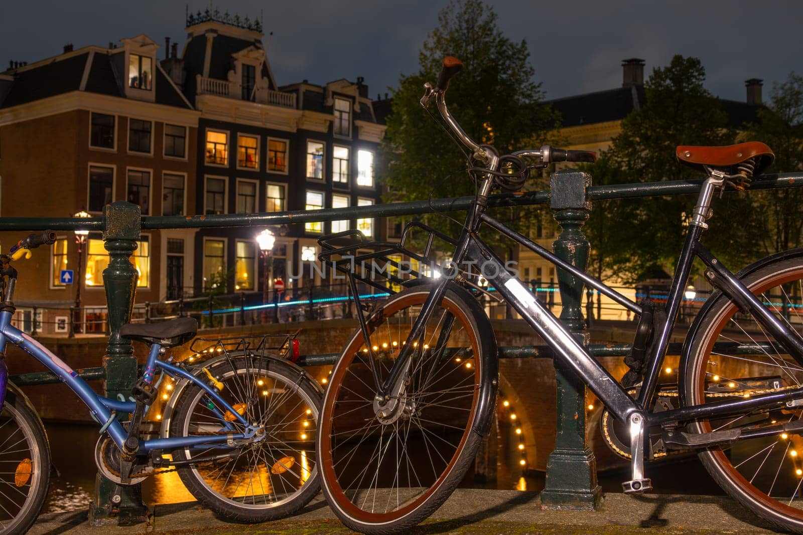 Netherlands. Night on the Amsterdam Canal. Adult and children's bikes are parked near the fence