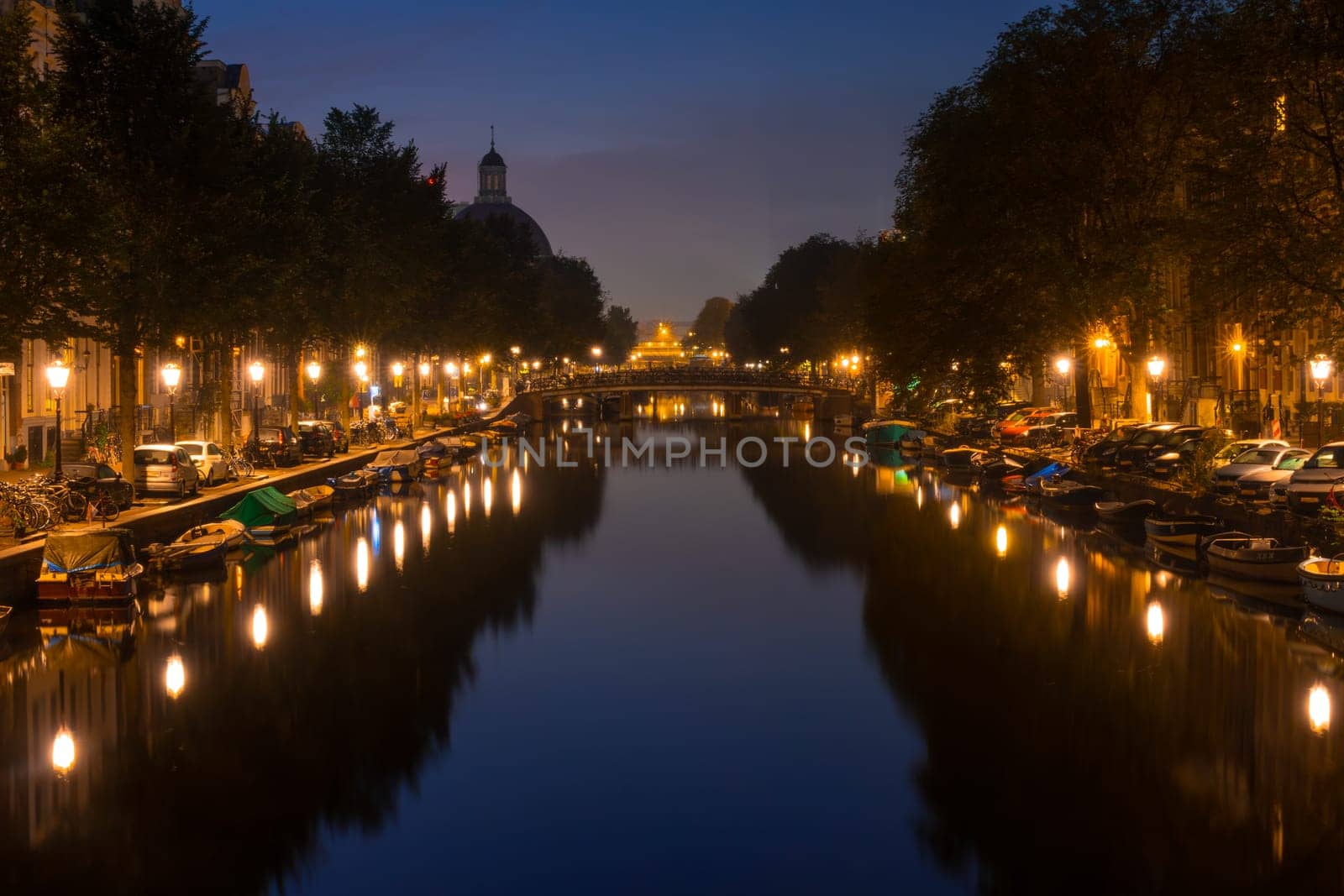 Netherlands. Summer night on the Amsterdam canal. Lanterns and parked cars on the embankments. Boats moored along the banks of the canal