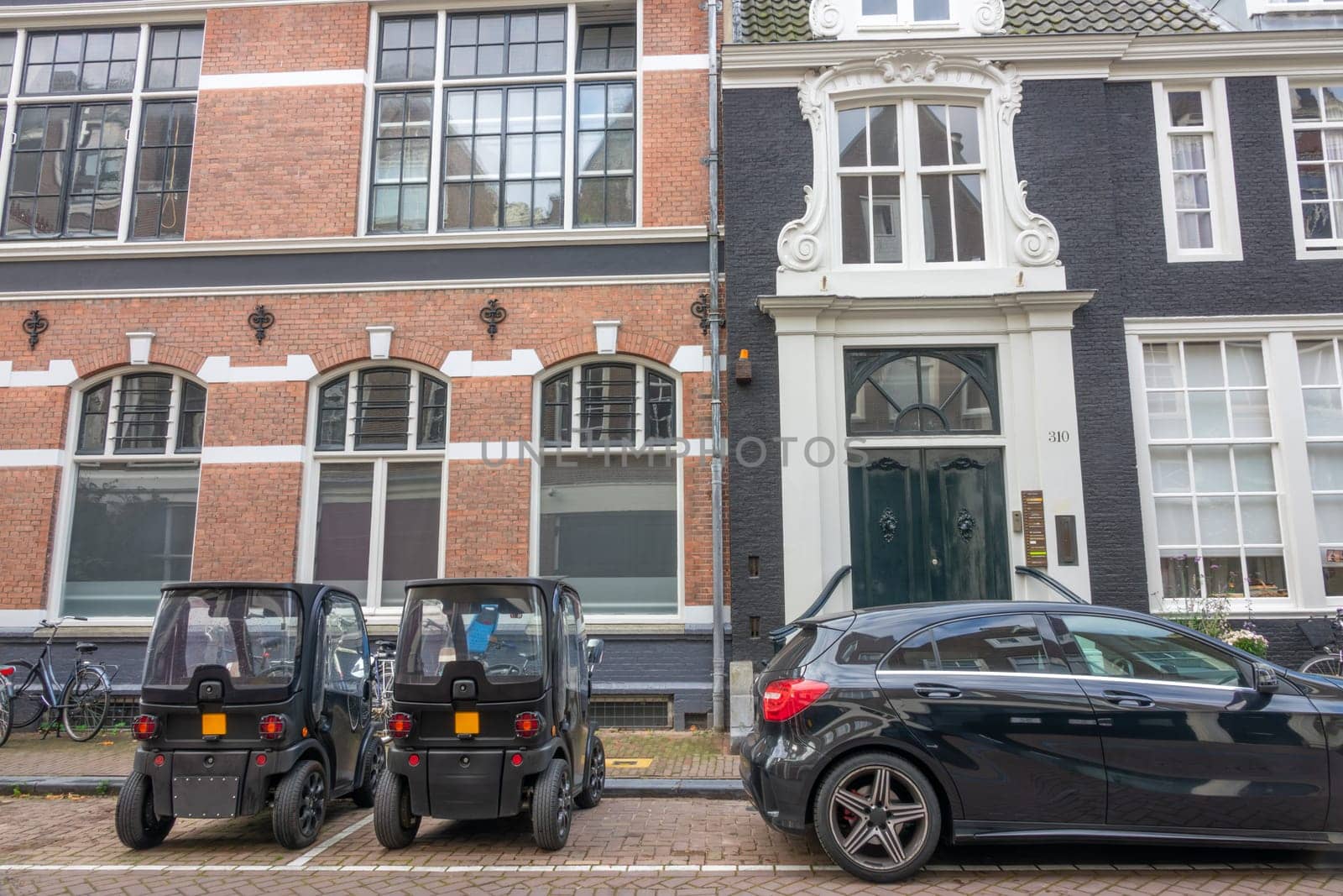 Netherlands. Small cobbled street in Amsterdam. Two mini cars are parked in front of the facade of authentic houses