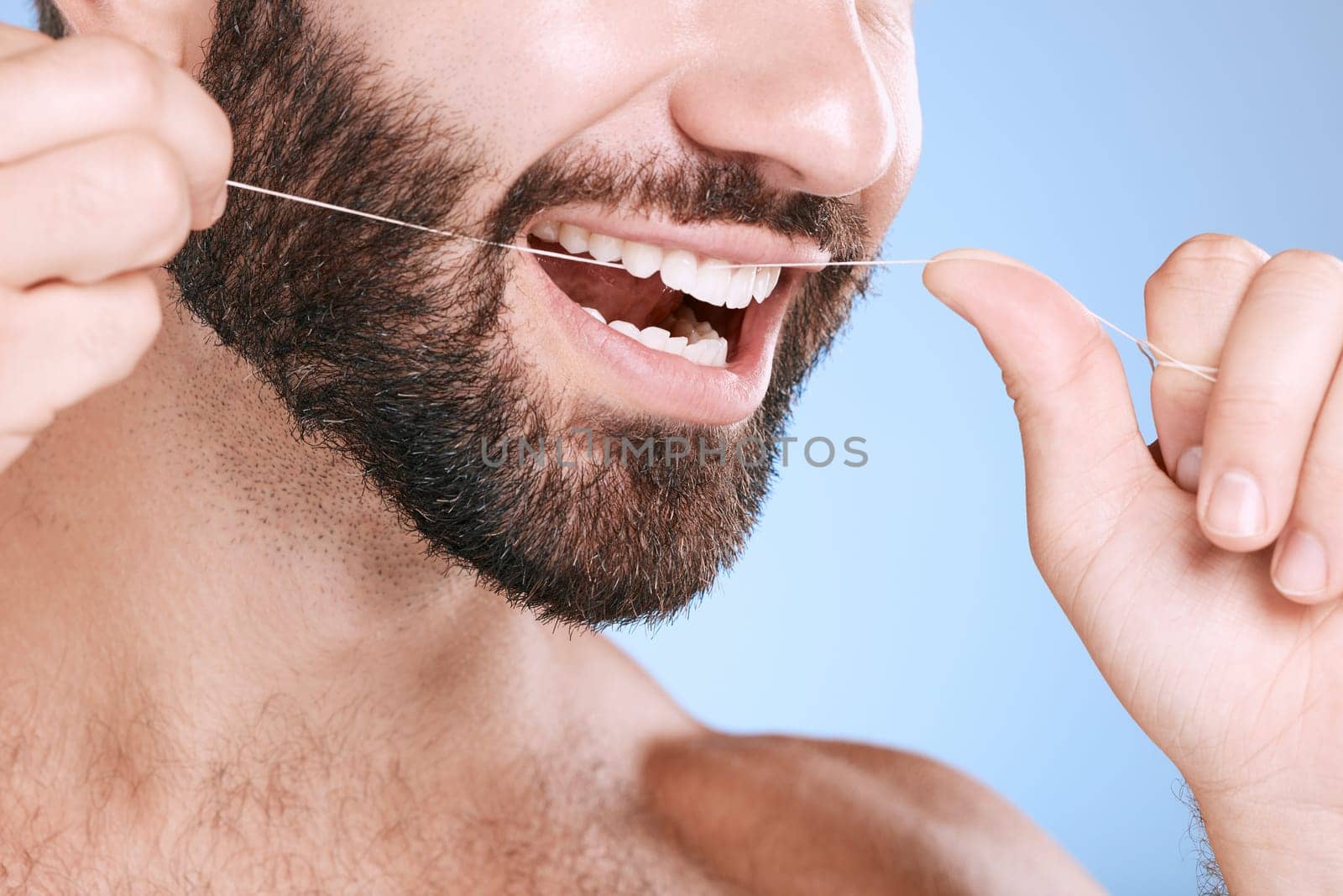 Dental, floss and oral hygiene with a man in studio on a blue background cleaning his teeth for healthy gums. Dentist, healthcare and mouth with a young male flossing to remove plague or gingivitis.