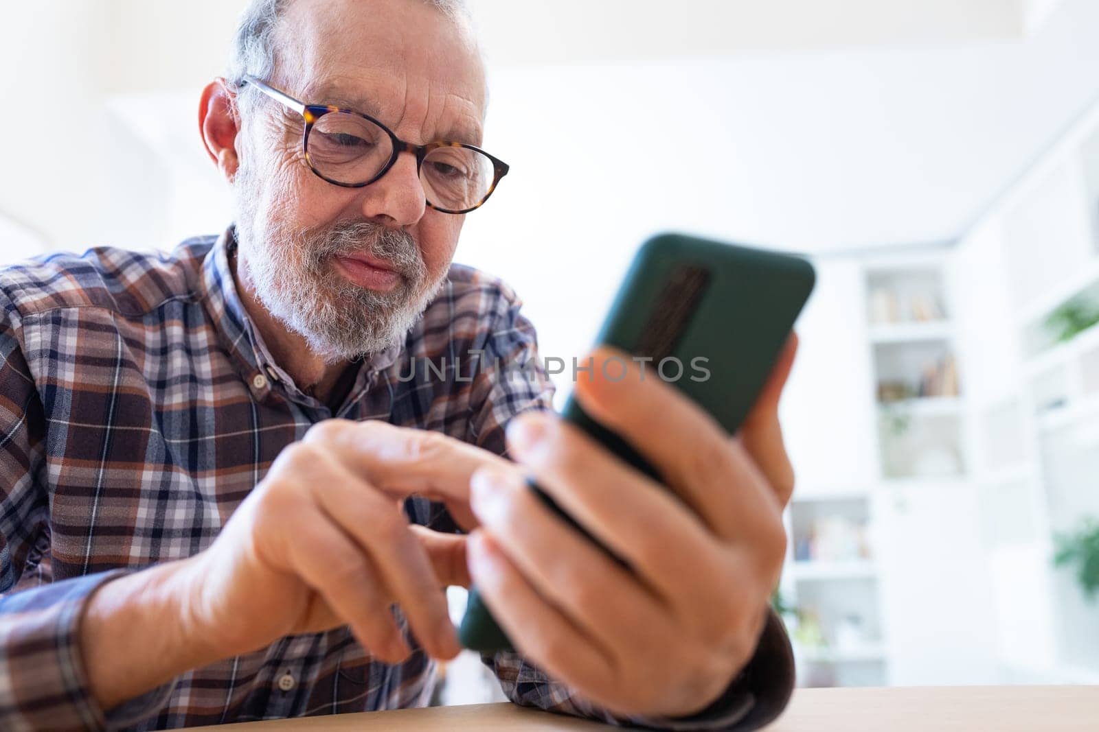 Mature adult caucasian man using mobile phone at home office. Lifestyle and technology.