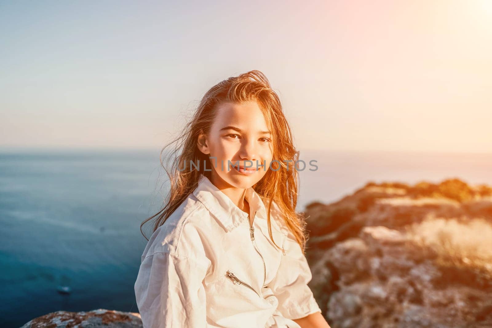 Brown-haired young romantic teenager girl corrects long hair on beach at summer evening wind