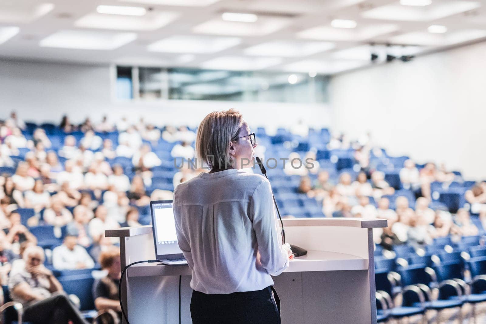 Female speaker giving a talk on corporate business conference. Unrecognizable people in audience at conference hall. Business and Entrepreneurship event. by kasto