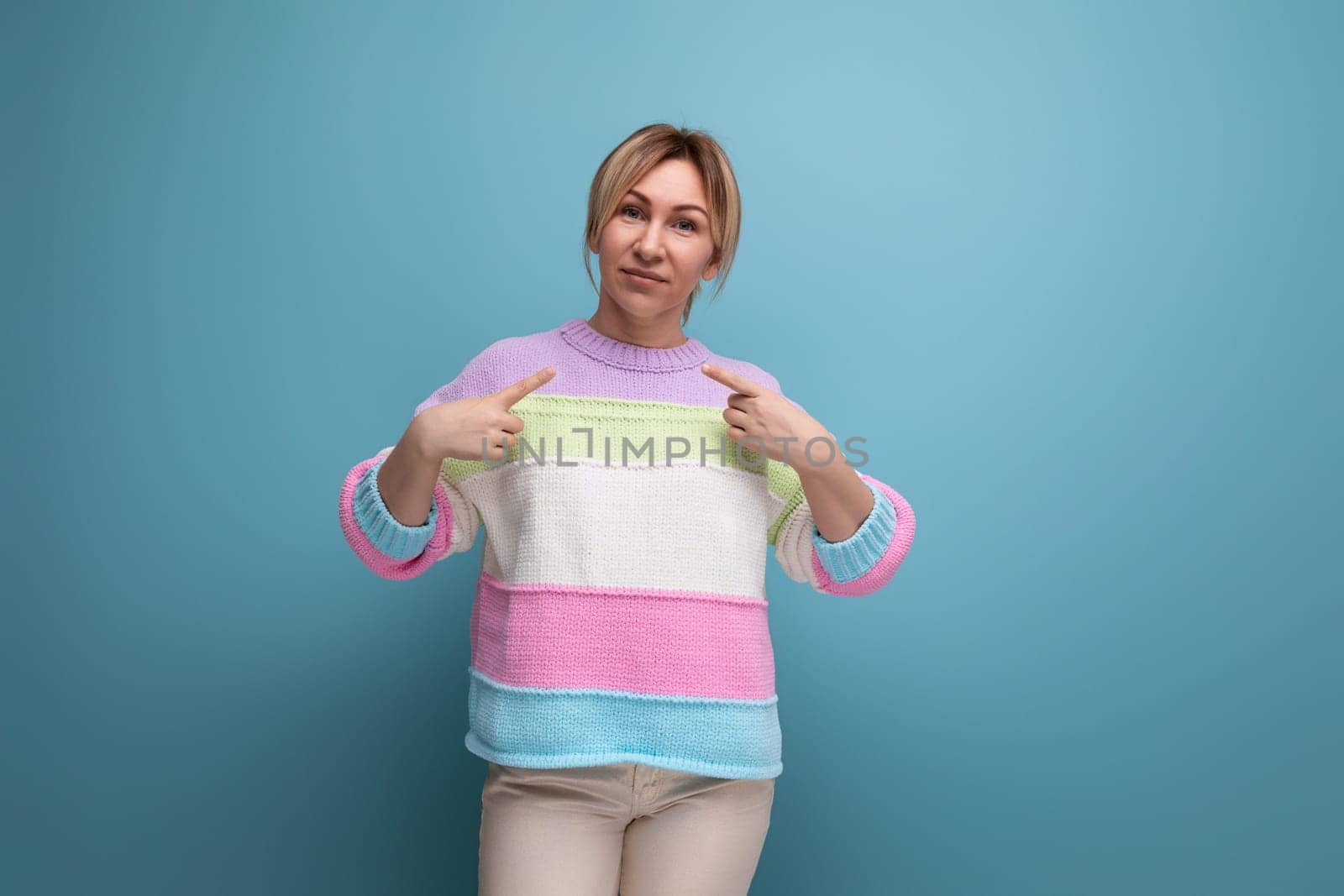 attractive blond woman in a casual look shows her hands at herself on a blue background.
