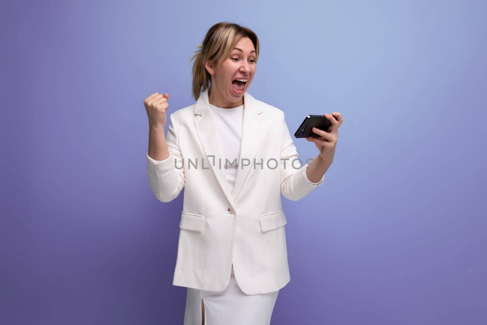 joyful young caucasian blondie lady in elegant jacket holding smartphone with mockup.