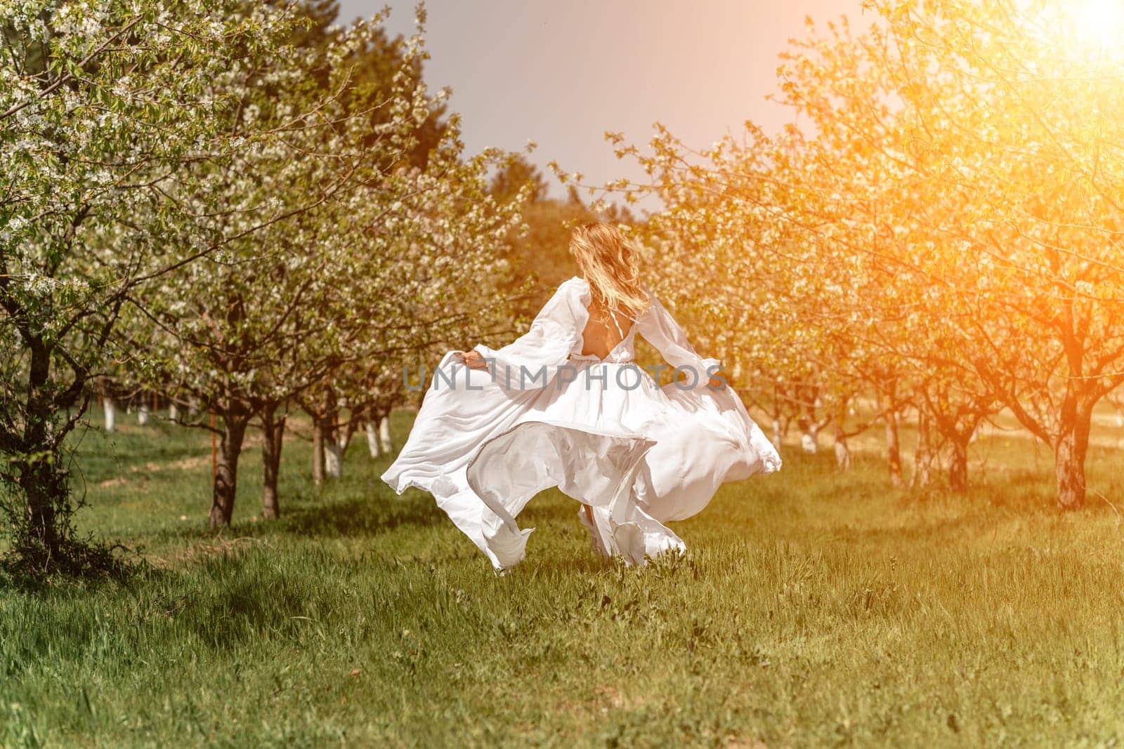 Woman white dress park. A woman in a white dress runs through a blossoming cherry orchard. The long dress flies to the sides, the bride runs rejoicing in life. by Matiunina