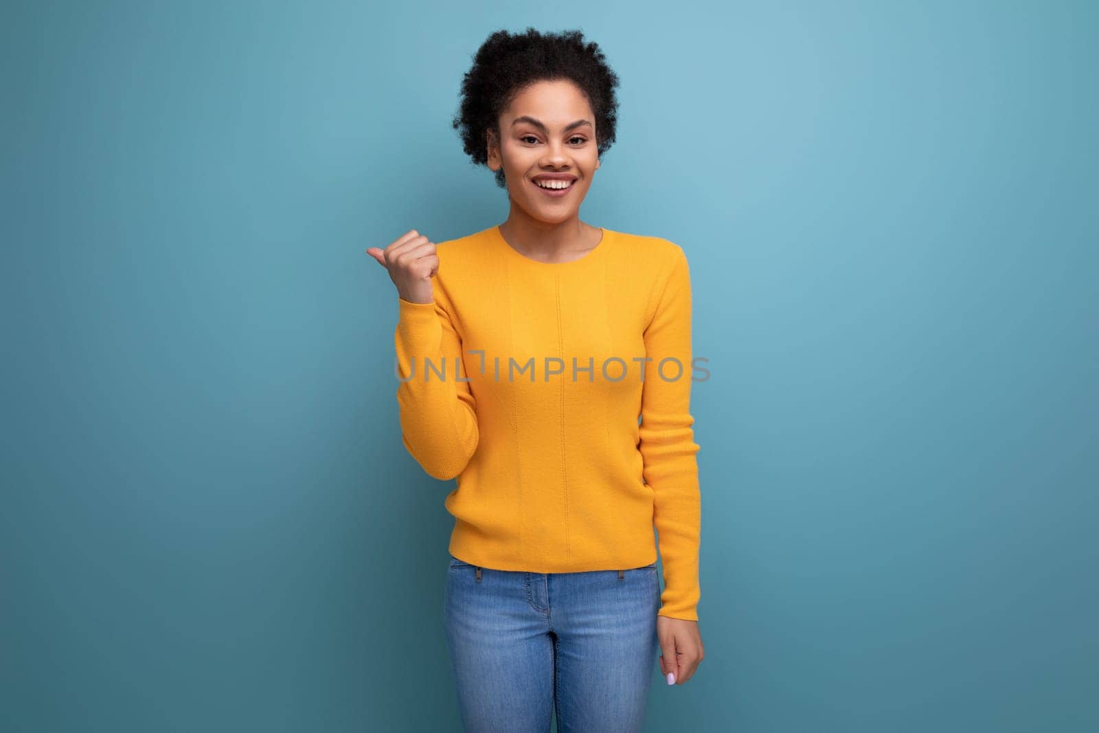 joyful young hispanic woman with black curly hair in a yellow jacket on a blue background.