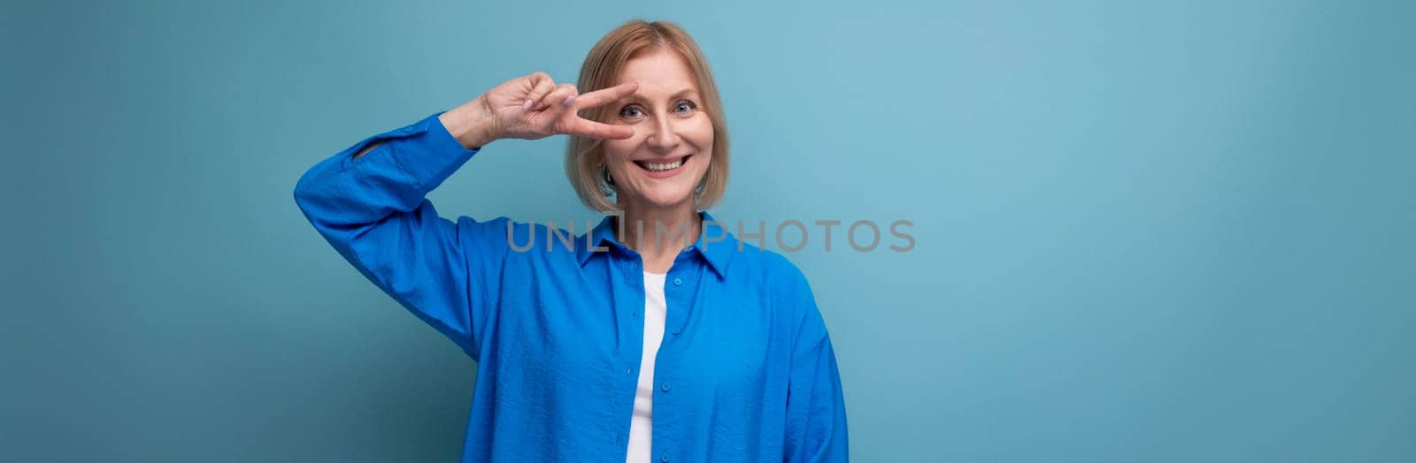 close-up of a charming mature woman in a blue shirt on a blue background with copy space.