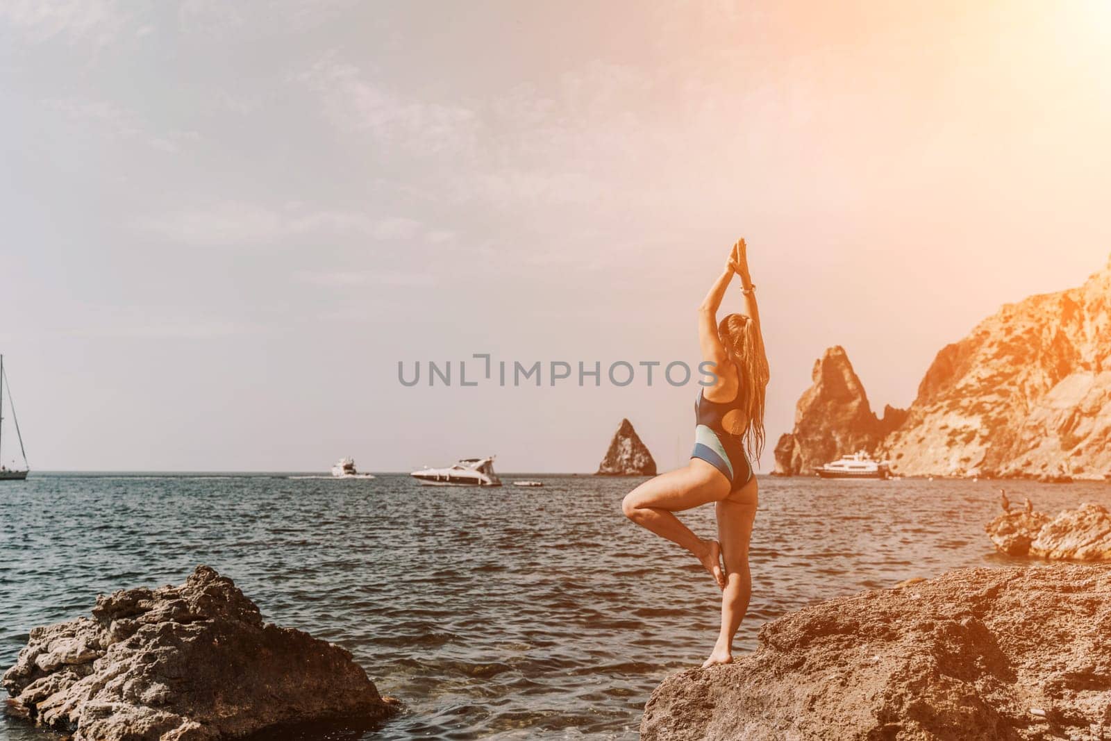 Yoga on the beach. A happy woman meditating in a yoga pose on the beach, surrounded by the ocean and rock mountains, promoting a healthy lifestyle outdoors in nature, and inspiring fitness concept