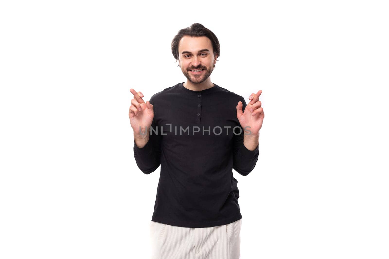 young handsome brunet european masculine man in black sweater crossed his fingers.