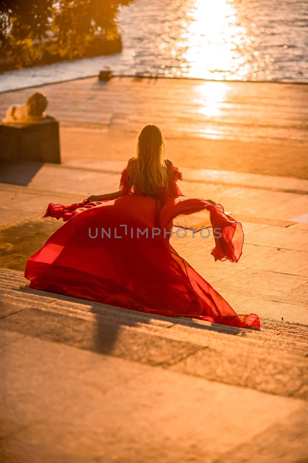 Sunrise red dress. A woman in a long red dress against the backdrop of sunrise, bright golden light of the sun's rays. The concept of femininity, harmony