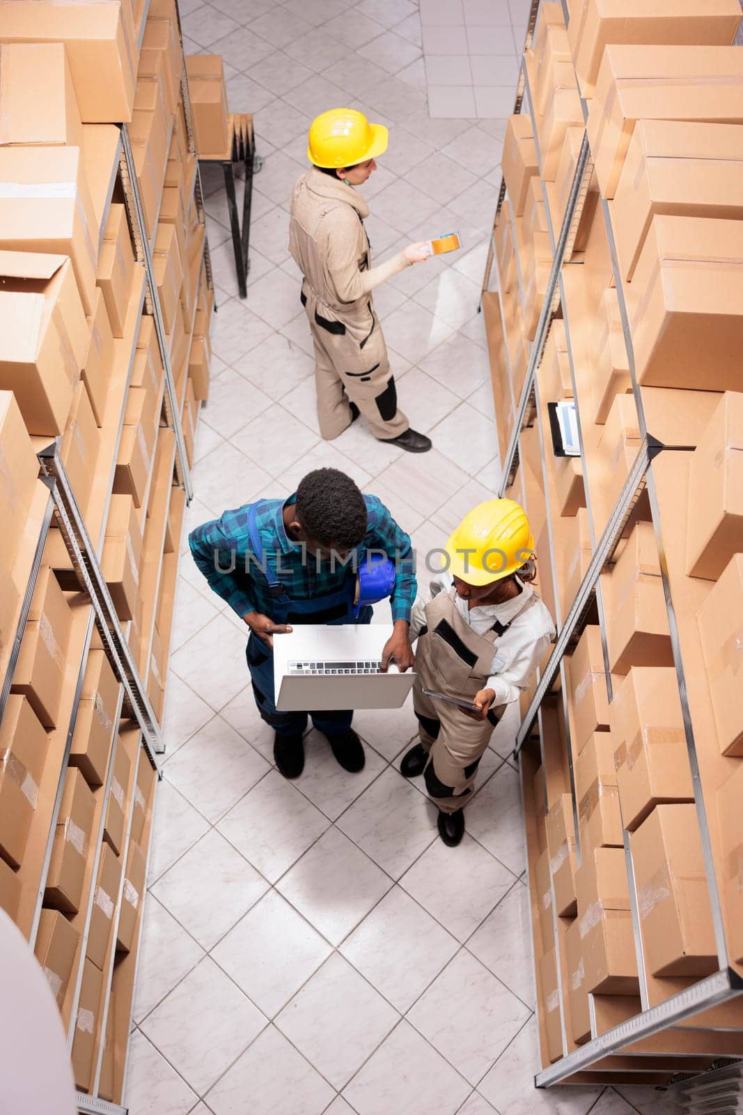 Storage room employees checking parcel delivery invoice on laptop. Warehouse managers diverse young team packing cardboard boxes for sending and doing merchandise inventory top view