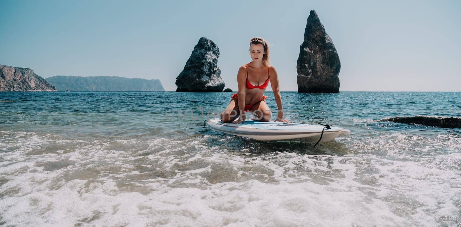 Close up shot of beautiful young caucasian woman with black hair and freckles looking at camera and smiling. Cute woman portrait in a pink bikini posing on a volcanic rock high above the sea