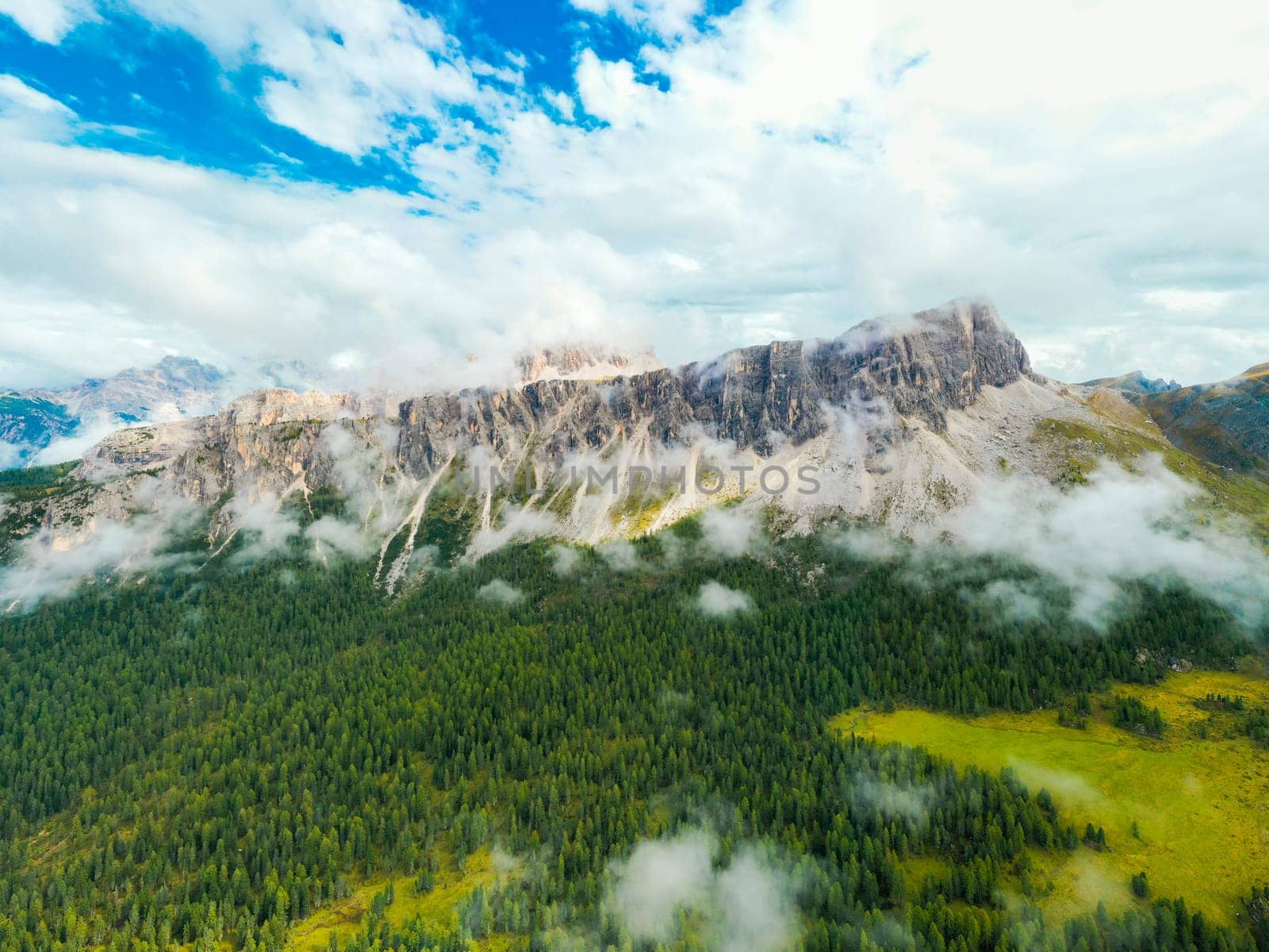 Panoramic view of breathtaking beauty of Rocky Dolomite Alps, where the summit disappears amidst of clouds, while a vibrant green forest flourishes at the foot of this majestic mountain.