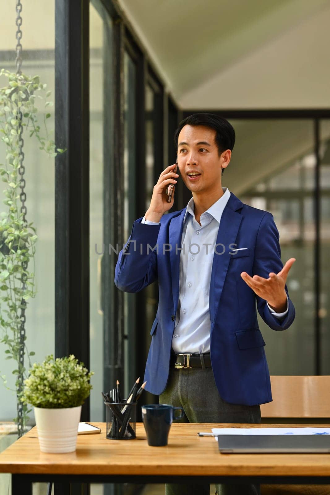 Portrait of successful financier investor answering or giving consultation to customer on mobile phone near office window.