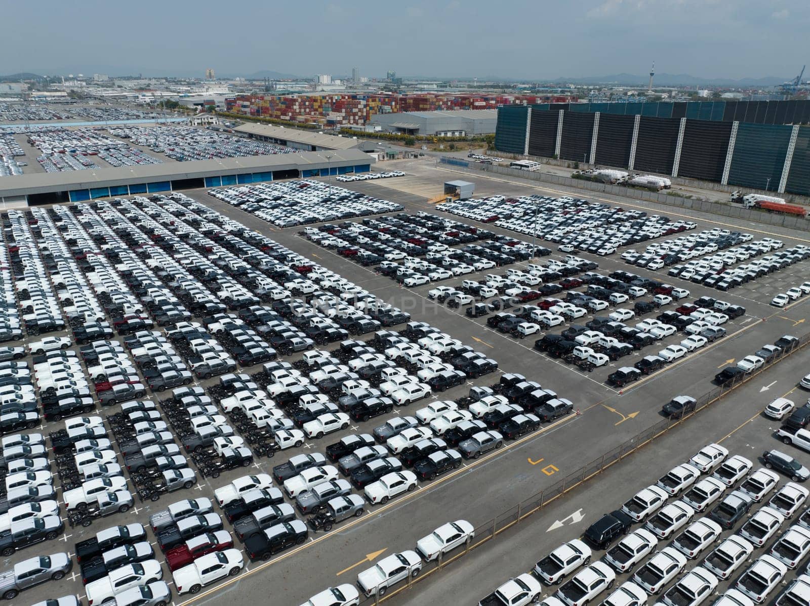 Aerial view of new cars stock at factory parking lot. Above view cars parked in a row. Automotive industry. Logistics business. Import or export new cars at warehouse. Big parking lot at port terminal by Fahroni
