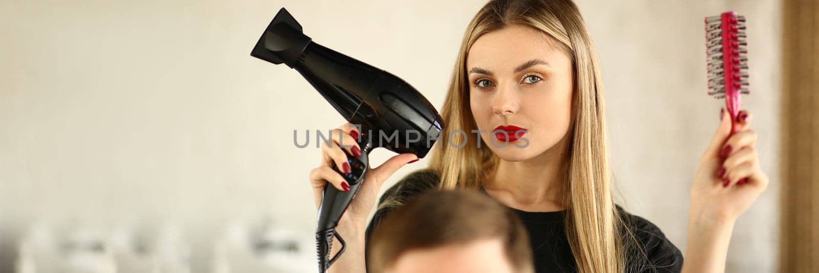 Woman hairdresser is holding hair dryer and hairbrush man is sitting in barbershop chair. Stylish trendy men's hairstyles and styling concept