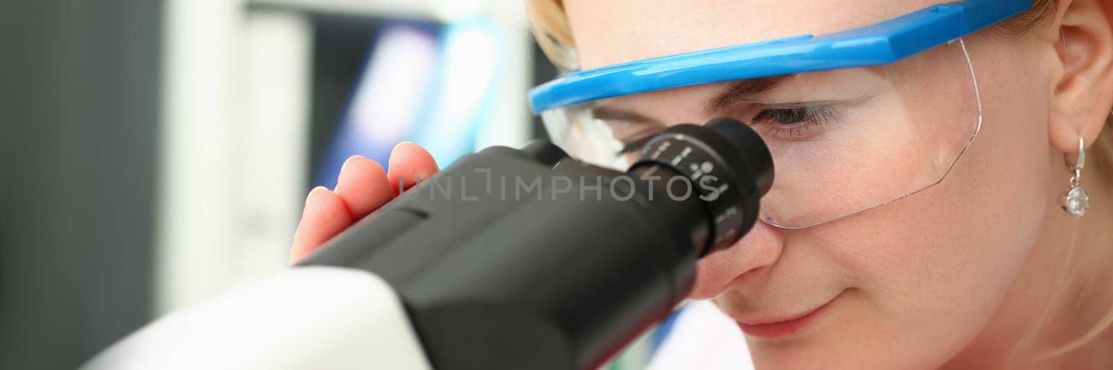 Portrait of focused female scientist looking through microscope in laboratory. Young scientist doing medical research