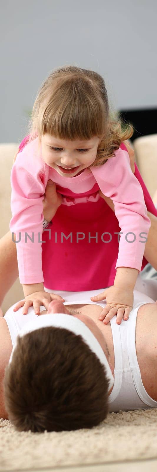 Joyful young father man lying on carpet floor lifting excited happy little daughter at home by kuprevich