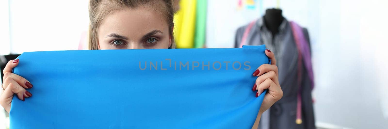 Portrait of smart hardworking woman covers fabric with face. Seamstress working on important project and fashion workshop concept