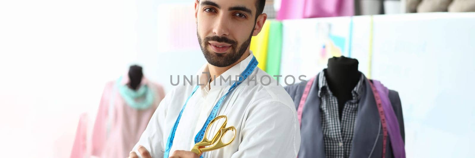 Smiling handsome fashion designer with scissors standing next to mannequin at workplace. Male fashion designer stylist concept